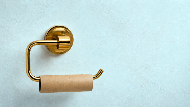 Empty cardboard toilet paper roll on a gold metal dispenser. Bathroom fixture on a light blue textured wall. Concept of running out of supplies. Copy space for text
