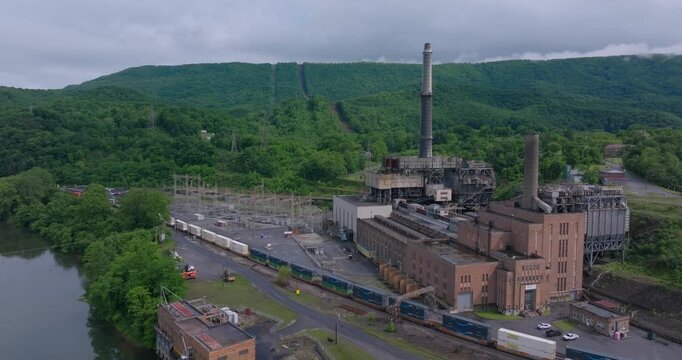 Aerial approach to Glen Lyn power plant beside river and rail corridor in Appalachia, drone ascend tilt down