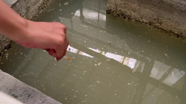 Worker checking wastewater acidity with a pH strip. Water treatment quality control and pollution monitoring in an industrial setting.
