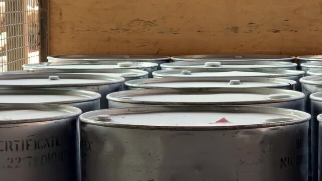 Metal drums containing industrial chemicals stacked in a storage facility. Manufacturing supplies, bulk materials, logistics, and industrial operations.
