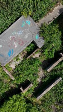 Chadwell Heath ZE1 gun emplacements seen from above as vertical format drone flies forward over overgrown WWII anti-aircraft battery remains, concrete hardstands and structures in east London, UK.