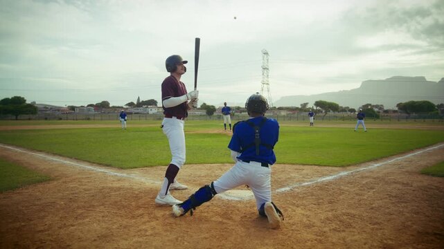 A batter stands ready at home plate as the pitcher throws a baseball. The catcher waits for the pitch in this action-packed game on the field.
