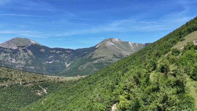 Panoramica mozzafiato di montagne maestose sotto un cielo blu limpido, circondate da rigogliosi pendii boschivi verdi in una giornata estiva soleggiata
