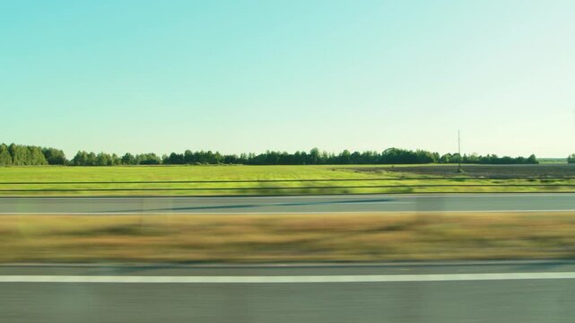 Dynamic perspective of road trip through beautiful summer rural landscape. Smooth motion blur across foreground and roadside emphasizes speed. Vibrant green field and clear blue sky define serene back