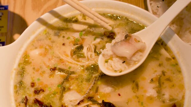 Close Up of Person Eating Spicy Asian Fish Soup with Chopsticks
