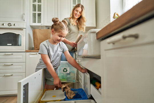 Mother looking at responsible girl throwing garbage in bin