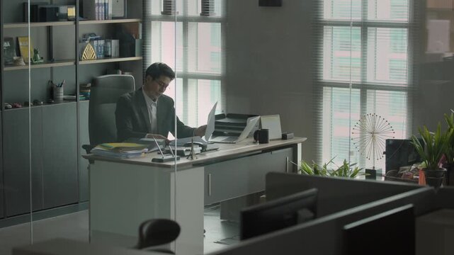 A businessman in a suit sitting alone in a dark modern office at night with dim lighting creating a moody cinematic atmosphere.