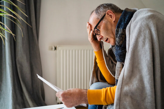 Worried man with head in hand looking at heating bill in home