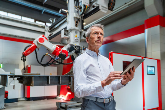 Factory manager holding tablet near industrial robot