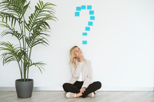Businesswoman sitting on the floor in office with question mark above her