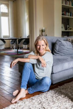 Portrait of smiling mature woman siiting barefoot on the floor in the living room
