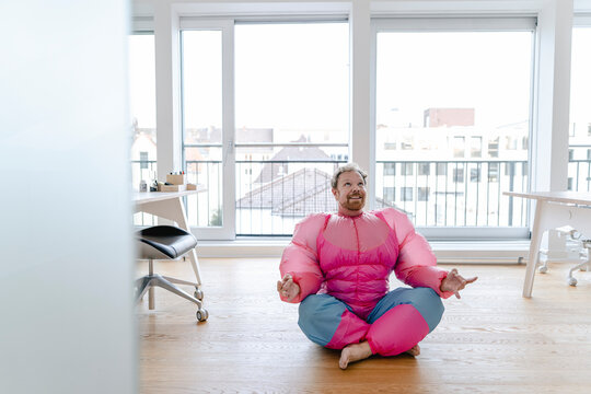 Businessman in office wearing pink bodybuilder costume practicing yoga