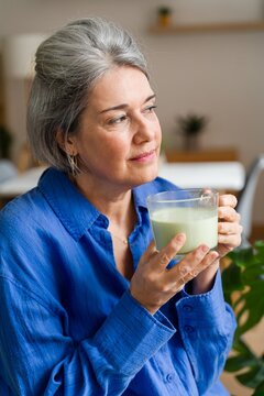 Thoughtful woman holding a glass mug of matcha latte at home