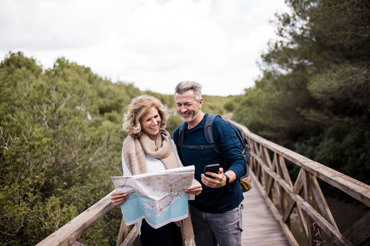 Smiling mature couple holding map standing on footbridge