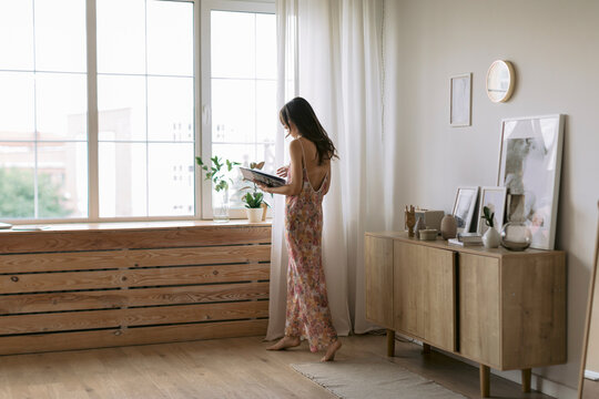 Young woman at the window at home holding a book