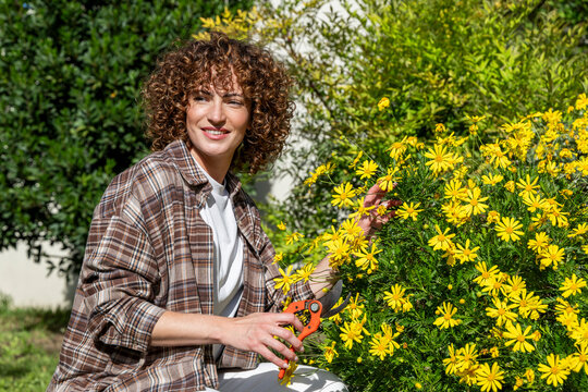 Smiling gardener pruning a yellow flower in sunny garden