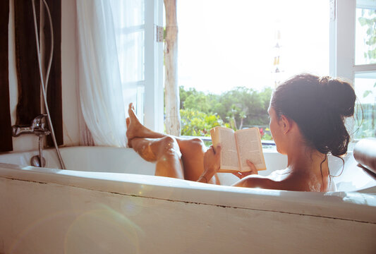 Woman relaxing in bathtub reading book