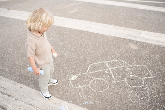 Child standing by chalk drawing of car on pavement