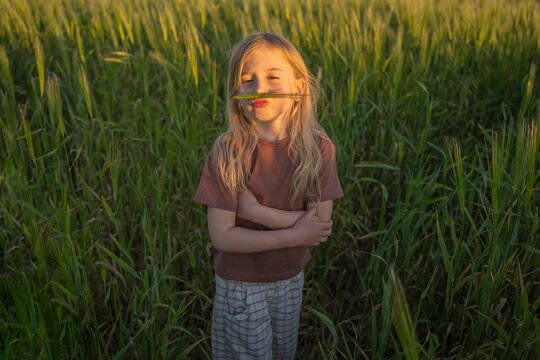 Girl holding grass like a mustache in a field at sunset