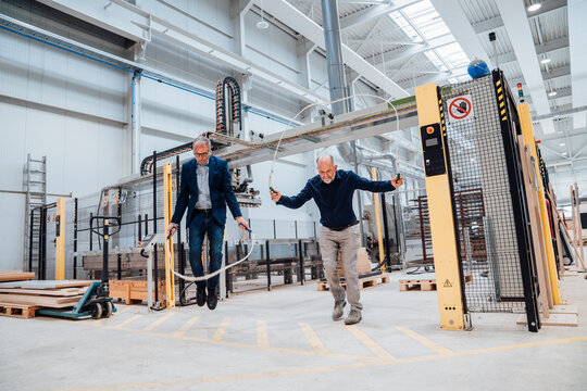 Two businessmen jumping rope in a factory setting demonstrating teamwork and innovation
