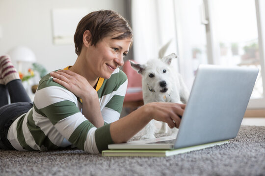 Smiling woman lying on the floor using laptop