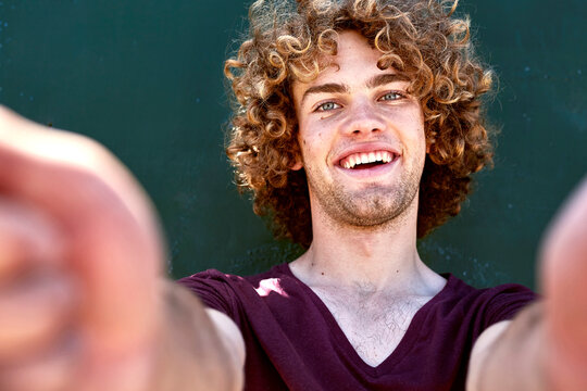 Portrait of laughing young man with curly hair in front of a green wall