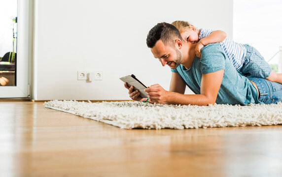 Happy father and daughter lying on rug using digital tablet