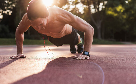 Shirtless man exercing push ups on sport field