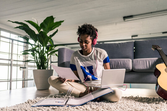Young woman at home with headphones, laptop and documents next to guitar