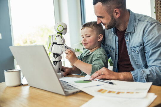 Smiling man looking at son playing with robot at home