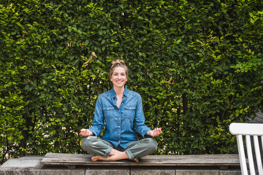 Portrait of woman meditating on bench in front of hedge