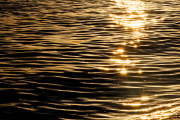 Horizontal abstract view of sparkling golden sunset reflections on dark ocean ripples. © MaxSangkaew