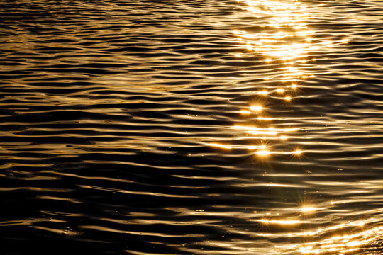 Horizontal abstract view of sparkling golden sunset reflections on dark ocean ripples.