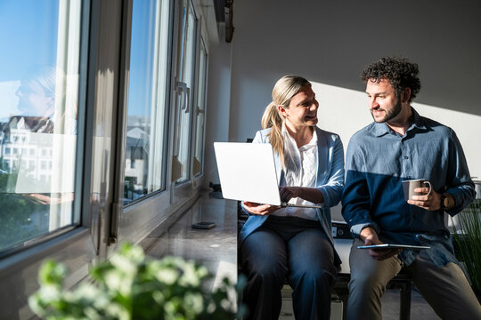 Colleagues discussing work with laptop by sunny office window