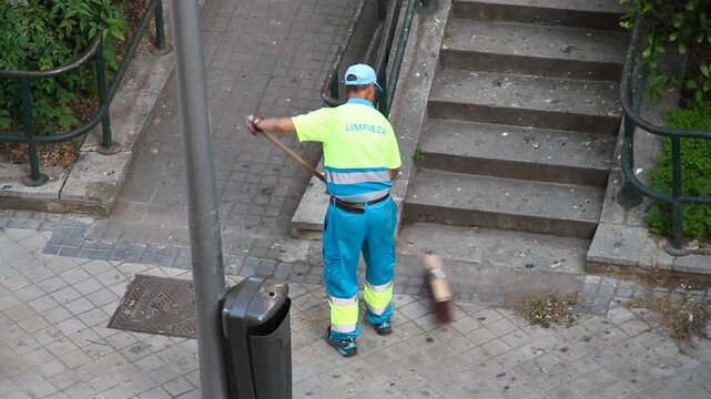 Barrendero limpieza calle ayuntamiento con escoba barriendo y limpiando opeario municipal acera v&iacute;a p&uacute;blica con uniforme