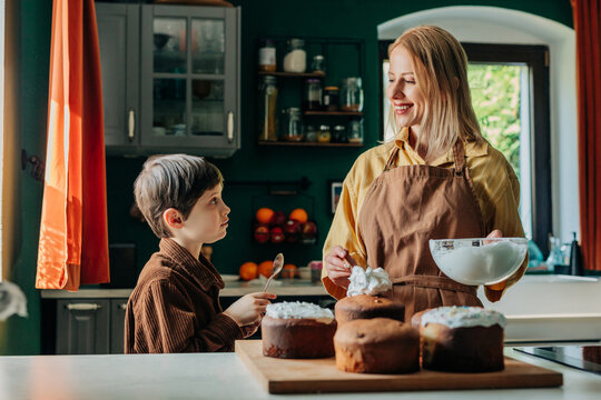 Smiling mother and son decorating Easter bread paska in kitchen