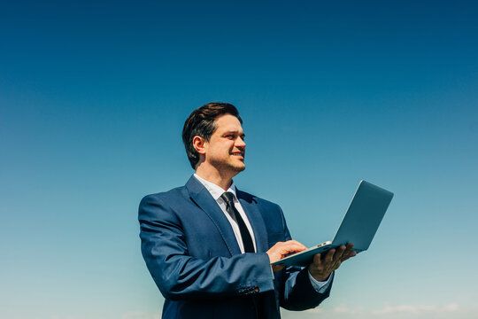 Businessman working on laptop computer outdoors against blue sky