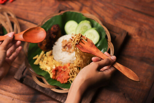 Hands lift noodles from a vibrant, rustic plate