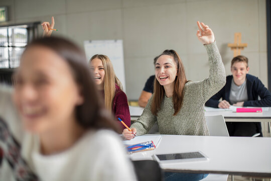 Happy teenage girls raising hands in class