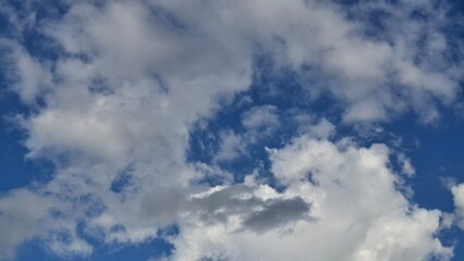 Fototapeta premium Beautiful white clouds moving across a bright blue sky, creating a peaceful natural background. Ideal for weather, nature, travel, environmental, and outdoor themed projects
