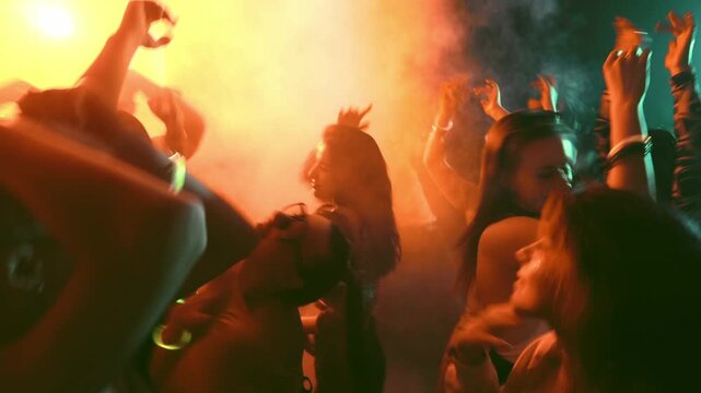 Dancing crowd at rave party with orange club lights and energetic nightlife mood. Concept of music festival, youth culture, party promo, nightlife video, dance event ads.