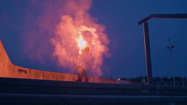 A skateboarder in adolescence performs a daring trick with a torch, creating a vibrant flare against the evening sky. The dynamic shot captures the energy and carefree spirit of youth culture.