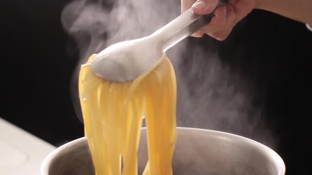 黒バックで茹でたパスタをトングであげる