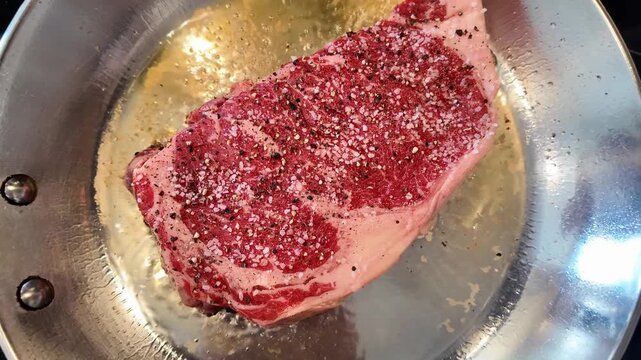 A seasoned ribeye steak sizzles in oil within a stainless steel pan representing the initial phase of gourmet beef preparation for a high quality home cooked dinner