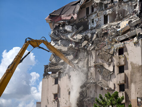Demolition crew uses heavy machinery to dismantle a building under a clear sky in an urban area