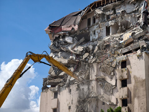 Demolition work is taking place on a building with heavy machinery removing debris in a city location during daylight hours
