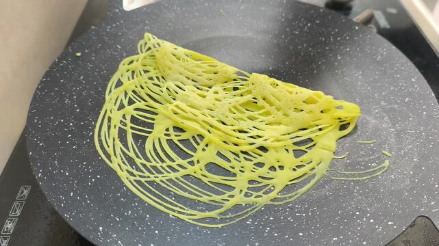 A chef expertly prepares traditional Malay roti jala. This net-like crepe is made from flour batter. It features a bright yellow color and is perfectly paired with savory curry.