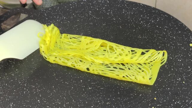 A chef expertly prepares traditional Malay roti jala. This net-like crepe is made from flour batter. It features a bright yellow color and is perfectly paired with savory curry.