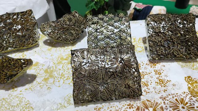 A craftsman creates a copper batik stamp. This traditional Malay art tool is dipped in hot wax to stamp patterns onto fabric. It saves time compared to hand-drawing.