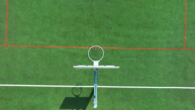 Cinematic aerial topdown shot of a basketball hoop and backboard on a green multisport court in Masuria, Poland. Suitable for sports, wellness, and youth activity themes.
